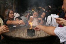 People lighting up some incense sticks in front of a temple